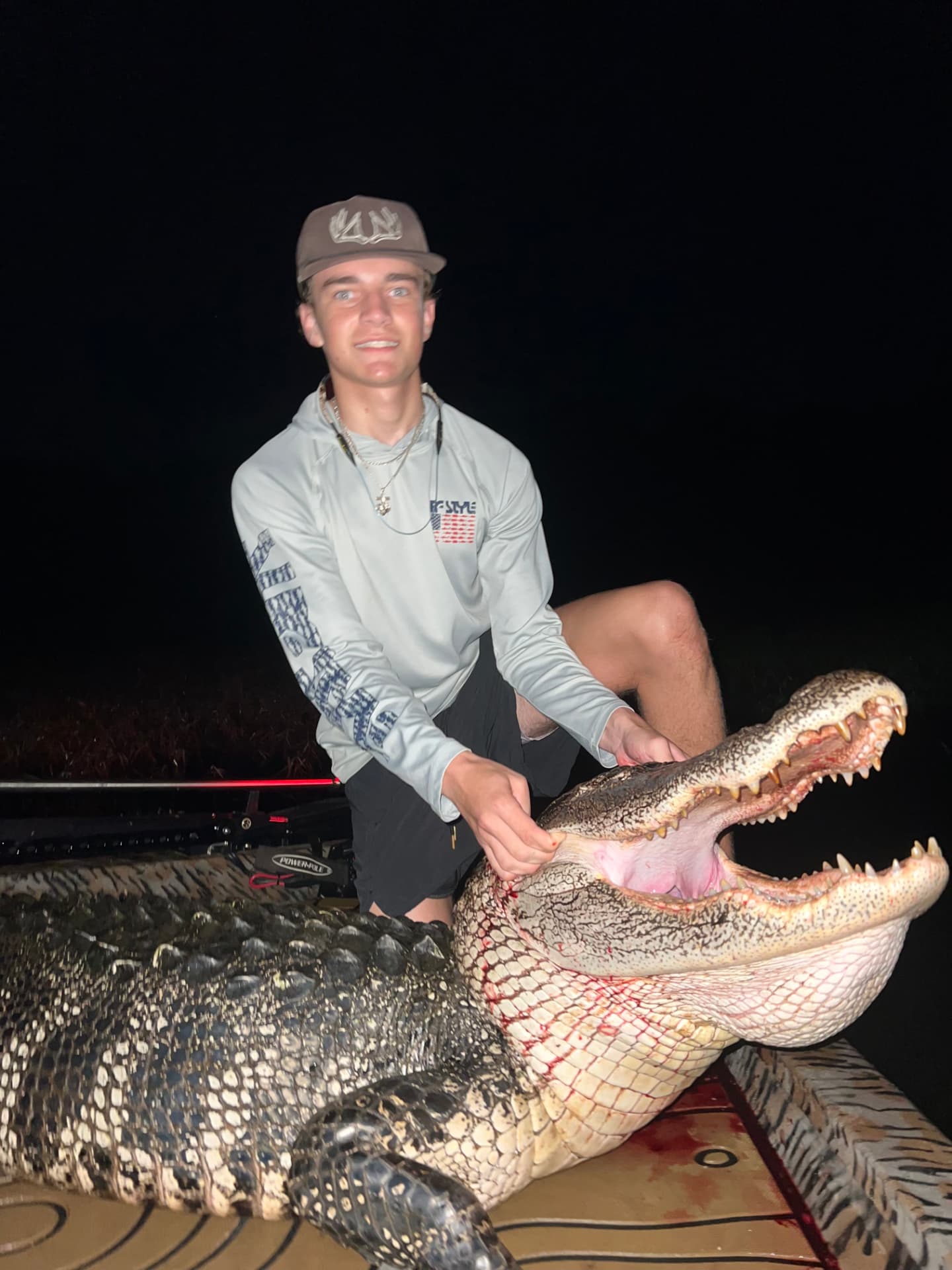 Young hunter in an Irons & Antlers cap on a boat at night with a harvested alligator